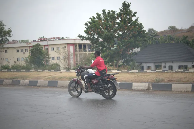 A motorcyclist riding along an urban street in Abuja, Nigeria, with the Aso Hills visible in the background