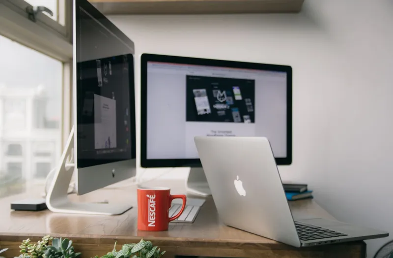 A silver MacBook open on a wooden table in a design studio setting